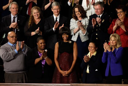 Michelle Obama standing and smiling while the people around her clap