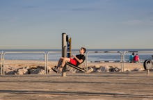 A man on the beach training cross fit on a sunny day, with the sea in the background