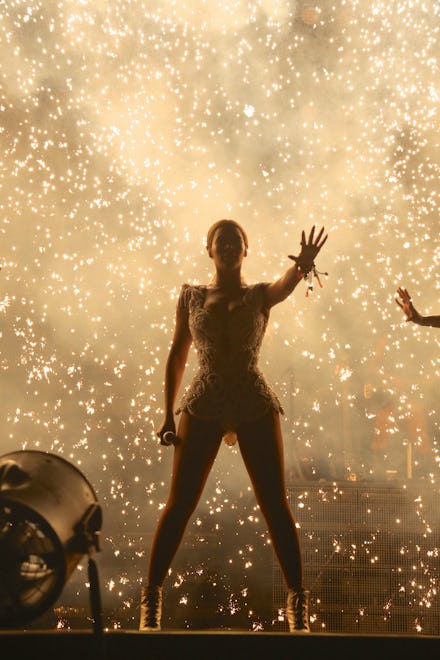 Beyoncé performing on stage in a gold dress, with sparks all around her
