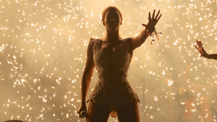 Beyoncé performing on stage in a gold dress, with sparks all around her  