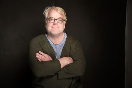 Philip Seymour Hoffman with his arms crossed, in front of a dark backdrop, with a slight grin on his...