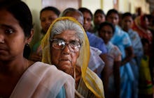 A cue for voting in India, with focus on two women at the front, looking tired and unamused. 