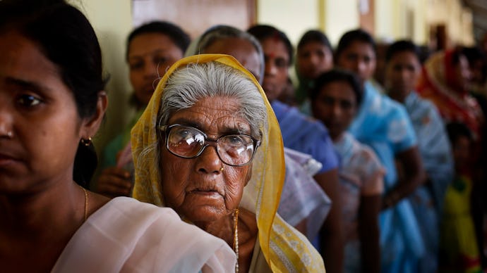 A cue for voting in India, with focus on two women at the front, looking tired and unamused. 