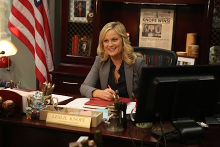 Amy Poehler as leslie knope sitting at her desk in the tv show parks and recreation