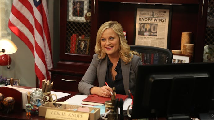 Amy Poehler as leslie knope sitting at her desk in the tv show parks and recreation 