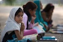 A little girl wearing a white hijab next to other 3 girls, reading a book