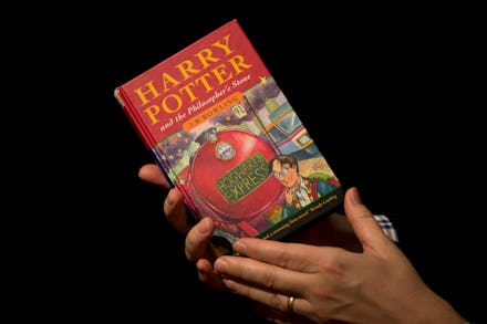 A person holding the book harry potter and the philosophers stone in front of a black background