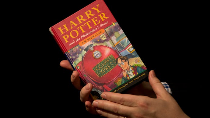 A person holding the book harry potter and the philosophers stone in front of a black background