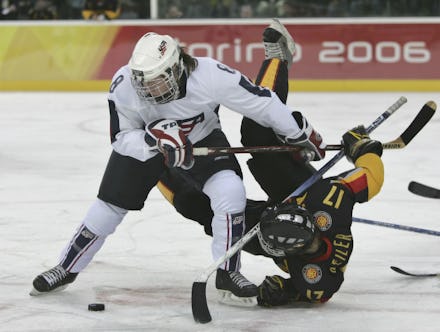 Two men playing hockey on ice, with one of them falling on his back, and another one reaching for th...