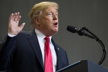 Donald Trump with his hand raised speaking into a microphone while standing at a podium