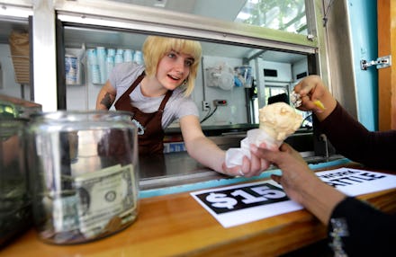 A low-wage working woman handing an ice cream cone through the delivery window while a tip jar stand...