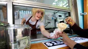 A low-wage working woman handing an ice cream cone through the delivery window while a tip jar stand...