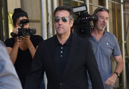 Michael Cohen wearing sunglasses with a people holding cameras walking behind him