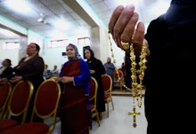 People sitting in a church in Iraq with the hand of a priest holding a gold cross in focus 