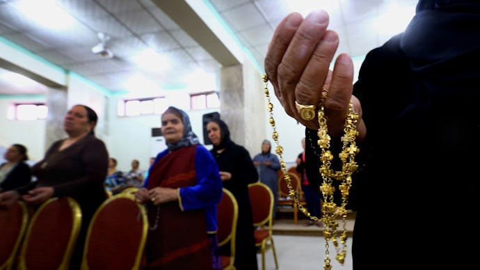 People sitting in a church in Iraq with the hand of a priest holding a gold cross in focus 