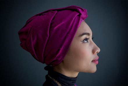 A closeup of Yuna in a red-purple hijab, winged eyeliner and pink lipstick turned sideways and looki...