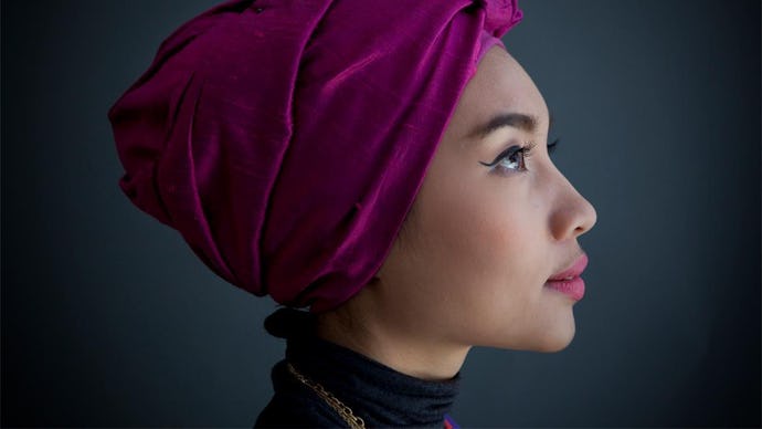 A closeup of Yuna in a red-purple hijab, winged eyeliner and pink lipstick turned sideways and looki...