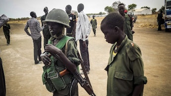 Two children and one of them is holding a helmet and a riffle in South Sudan