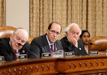 Four politicians sitting next to a large wooden desk with microphones in front of then