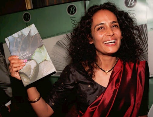 Arundhati Roy holding her book The God of Small Things, with a wide smile on her face. 