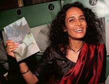 Arundhati Roy holding her book The God of Small Things, with a wide smile on her face. 