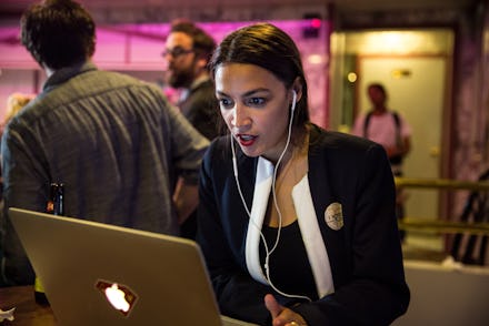 Alexandria Ocasio-Cortez using a laptop and wearing white earphones