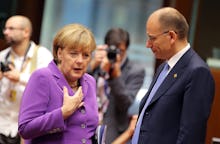 Angela Merkel in a pink outfit talking to another politician while journalists take photos