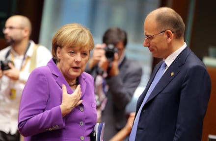 Angela Merkel in a pink outfit talking to another politician while journalists take photos