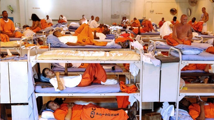 Prisoners laying in a cell in their bunk beds in orange jumpsuits