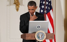 Barack Obama standing  next to a pedestal with a screen before giving a speech