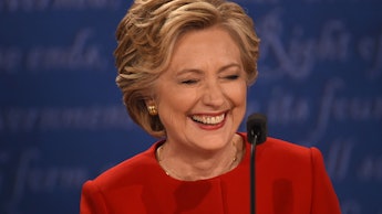 Hillary Clinton in a red suit laughing with a microphone in front of her