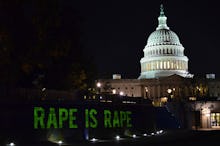 A sign that says rape is rape in front of the United States Capitol at night