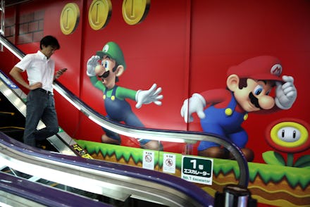 A man going down on escalator stairs with a large poster of Super Mario on a wall nest to the stairs