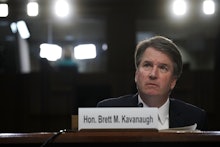Brett Kavanaugh sitting down behind a plaque with his name on it, lights shine behind him