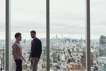 Two men standing in front of a large window overlooking the city behind them