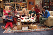 The cast of The Big Bang Theory sitting in the living room eating takeout in a scene of an episode