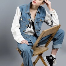 Hipster girl sitting on a wooden chair, in a denim outfit, showing how regular, unbothered outfits a...