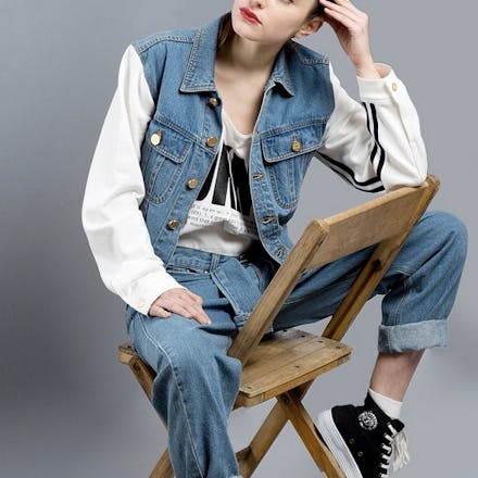 Hipster girl sitting on a wooden chair, in a denim outfit, showing how regular, unbothered outfits a...