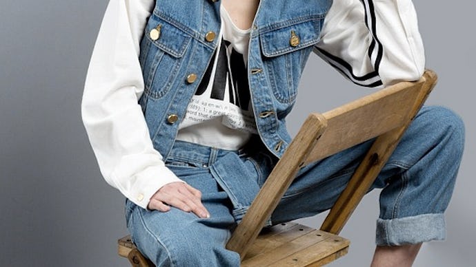Hipster girl sitting on a wooden chair, in a denim outfit, showing how regular, unbothered outfits a...