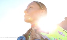 A woman standing in a blue jacket with the sun in the background