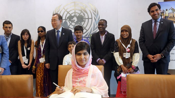 Malala Yousafzai sitting at the UN and writing in a book