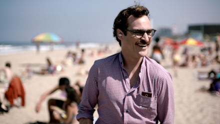 Joaquin Phoenix in a pink shirt walking on the beach during a sunny day