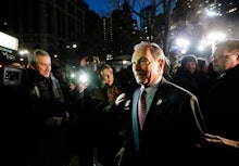 Mike Bloomberg walking while many reporters are taking photos of him with flashes