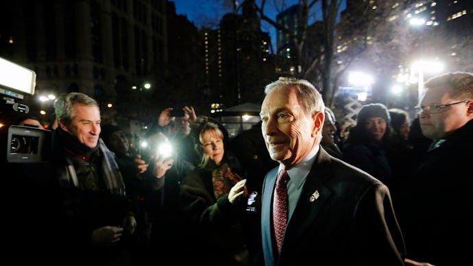 Mike Bloomberg walking while many reporters are taking photos of him with flashes