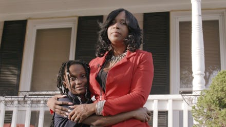 Tyrone West's sister, Tawanda Jones in a red suit next to her child in front of a house