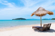 An empty beach on a sunny day with two lounge chairs and a straw sun protector