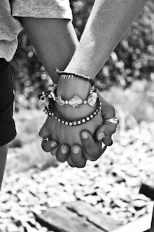 A black and white closeup of two Internet friends holding hands, one has three bracelets and the oth...
