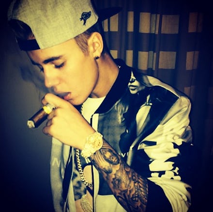 Justin Bieber smoking a cigar, holding it in his tattooed arm, looking down, trying to show off his ...