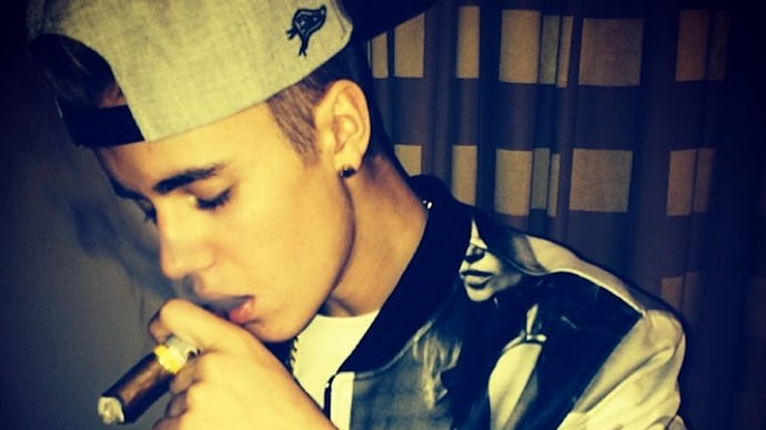 Justin Bieber smoking a cigar, holding it in his tattooed arm, looking down, trying to show off his ...