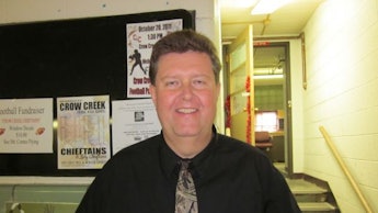 Patrick Jones in a black shirt and grey tie in a school hall